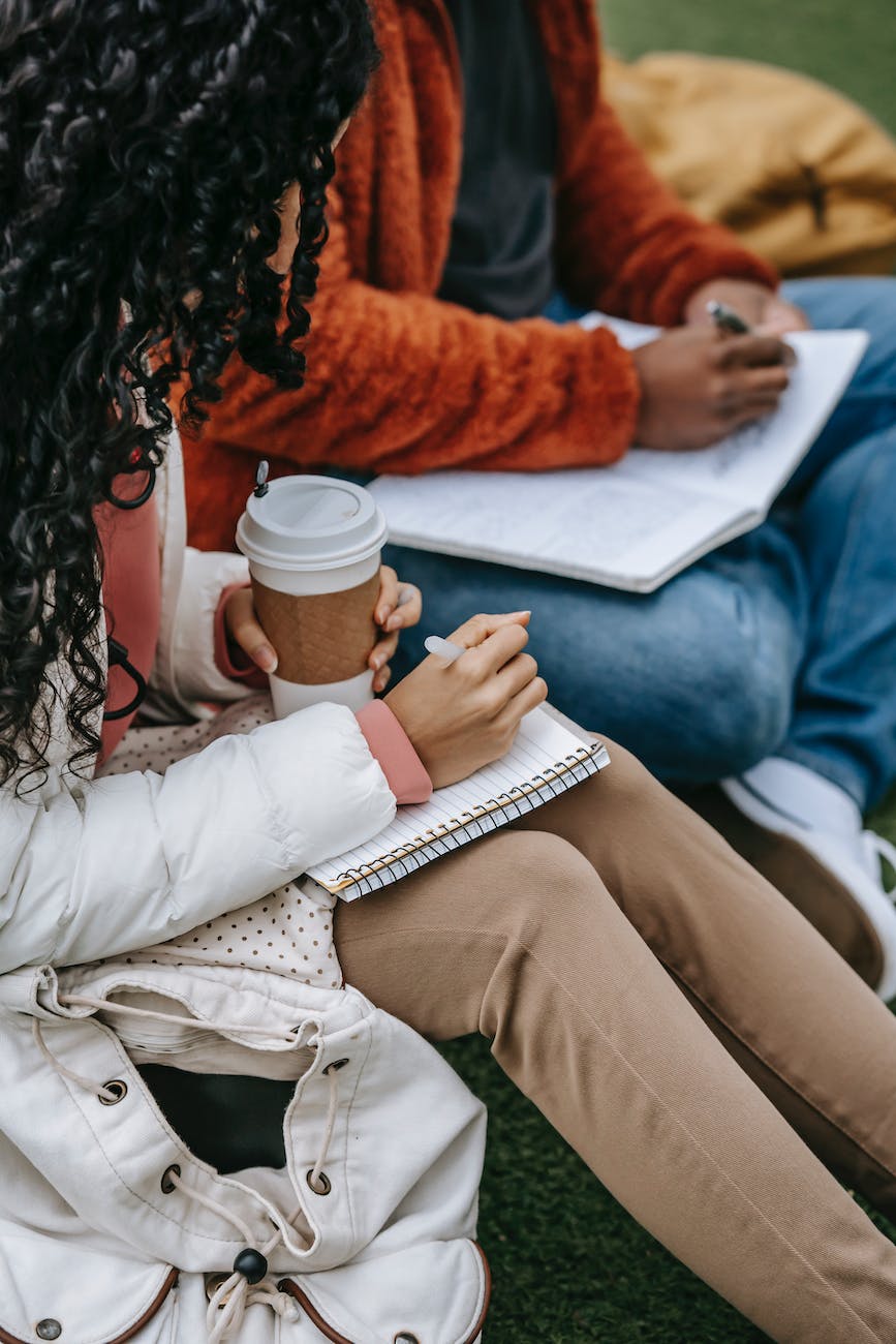 crop multiracial students writing in notebooks on street